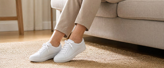 Relaxed crossed legs in clean white no-tie sneakers at home during foot recovery